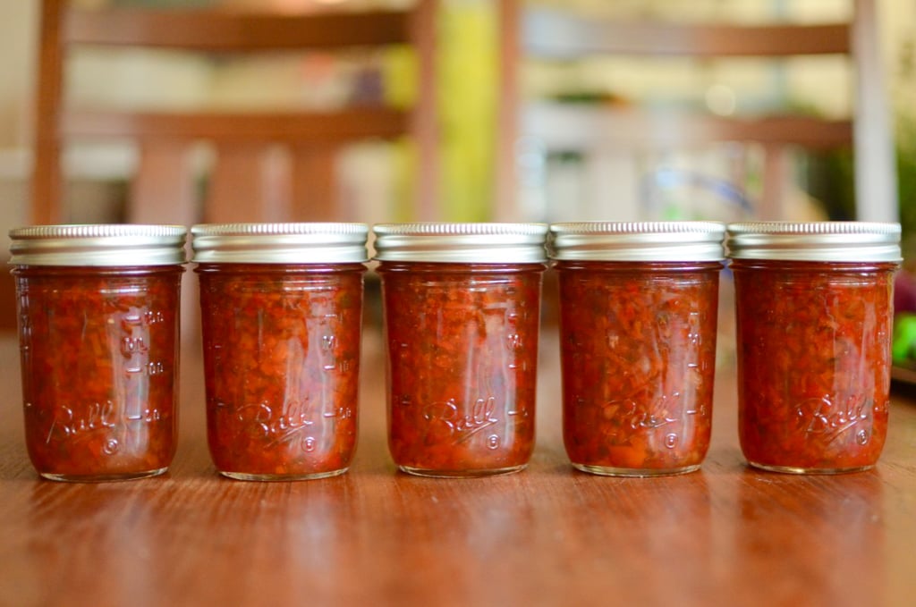 Five half pint jars of pepper jelly lined up on a table