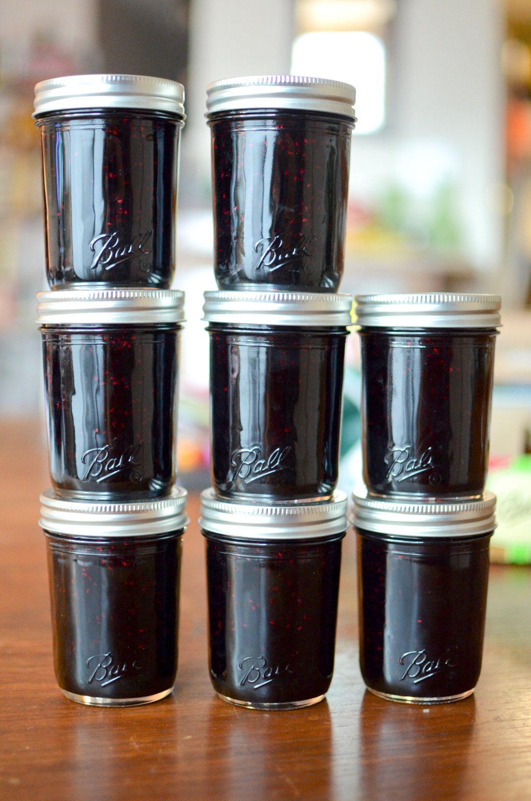 A vertical image of eight half pint jars of finished black raspberry jam. 