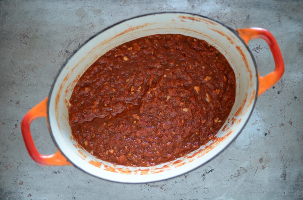 Chunky cooked harissa in an oval, orange dutch oven. 