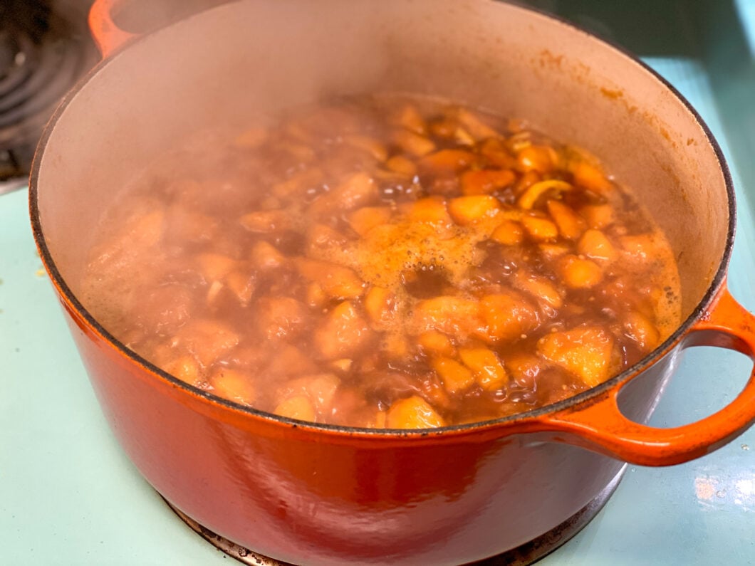 Lemon peach turmeric chutney in an orange Le Creuset pot, simmering on a turquoise stove. 