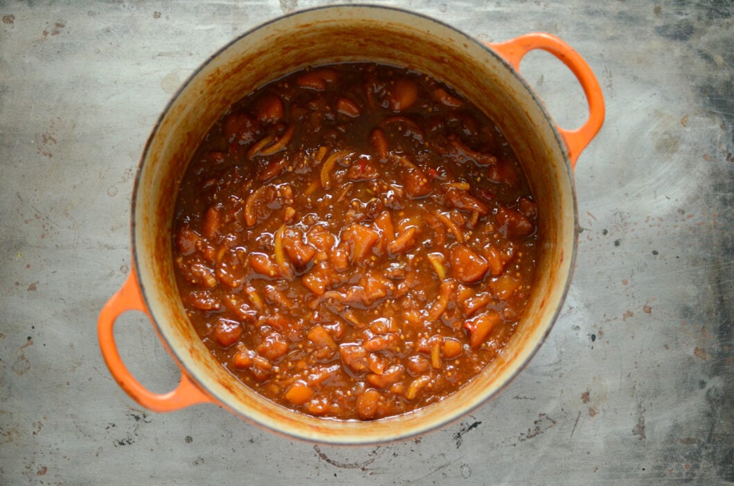 Cooked lemon peach turmeric chutney in an orange Le Creuset pot, sitting on a metal background. 