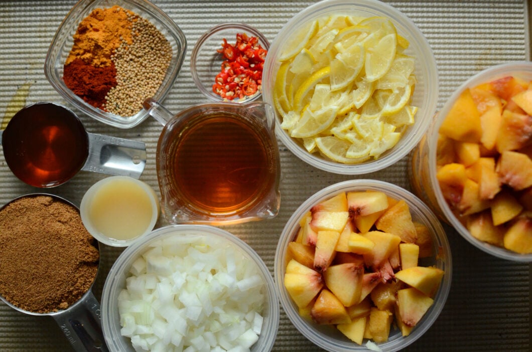 Chutney ingredients on a sheet pan. Chopped peaches, onions, lemons, chilies, apple cider vinegar, coconut sugar, honey, lemon juice, and spices. 