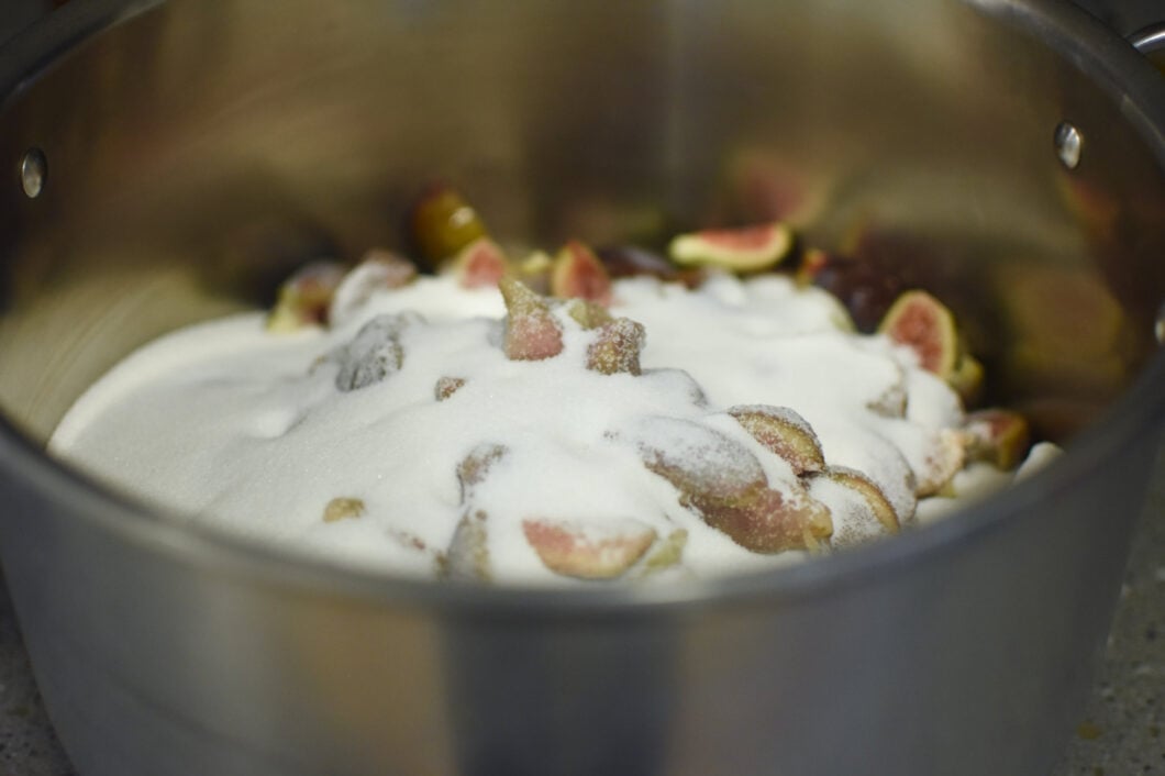 Quartered figs in a large pot, covered with white sugar.
